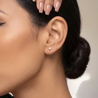 A person with dark hair in a low bun wears a small round diamond stud earring and displays nude-colored nail polish on their fingernails.