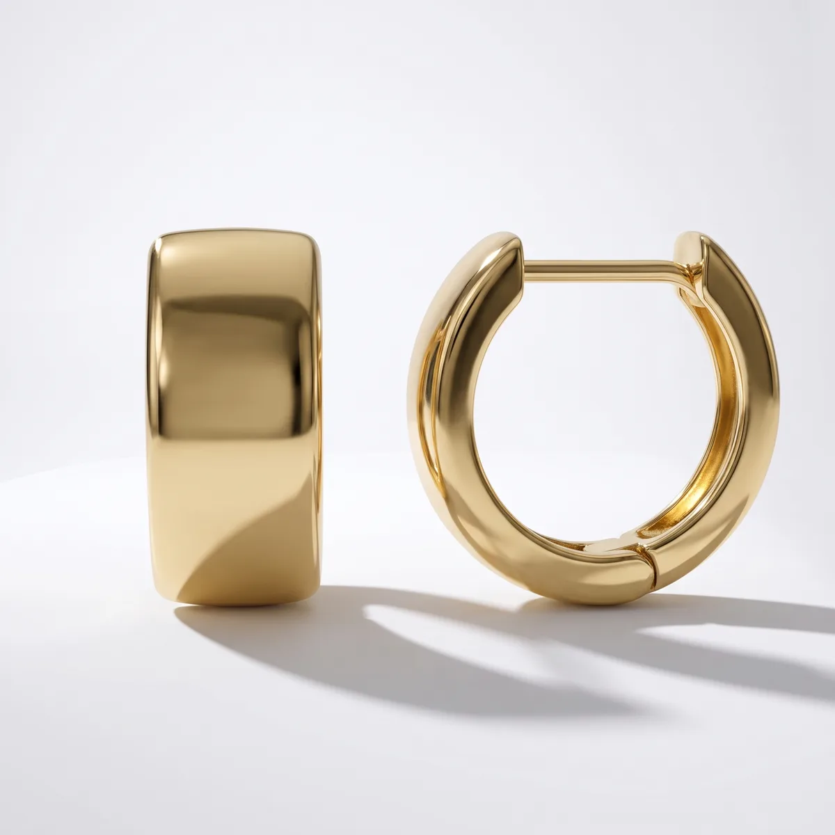 A pair of polished gold-toned chunky hoop earrings with hinged closures displayed on a white surface.