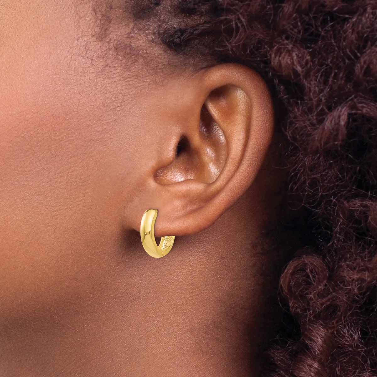 A person wearing a gold-toned chunky hoop earring in their earlobe, shown in profile with textured dark hair visible in the background.