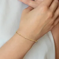 A delicate gold chain bracelet with small beaded details worn on a person's wrist against a white background.