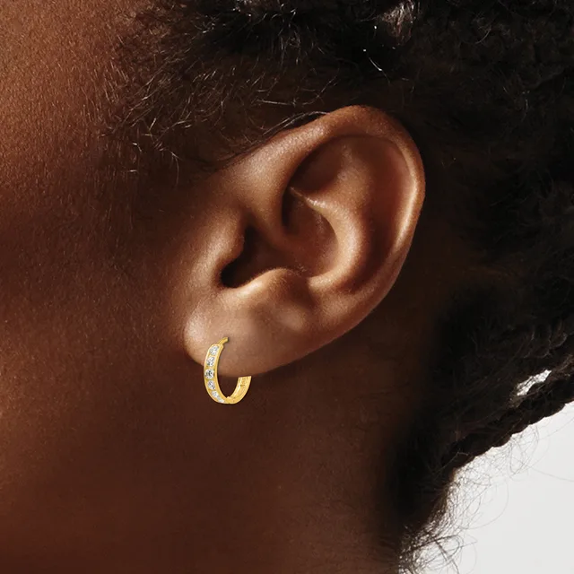 A gold hoop earring with a textured surface worn in the earlobe of a person with brown skin and dark hair.