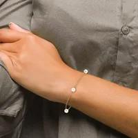 A person's arm wearing a gray button-up shirt displays two pearl bracelets and a delicate chain bracelet with a small pendant.