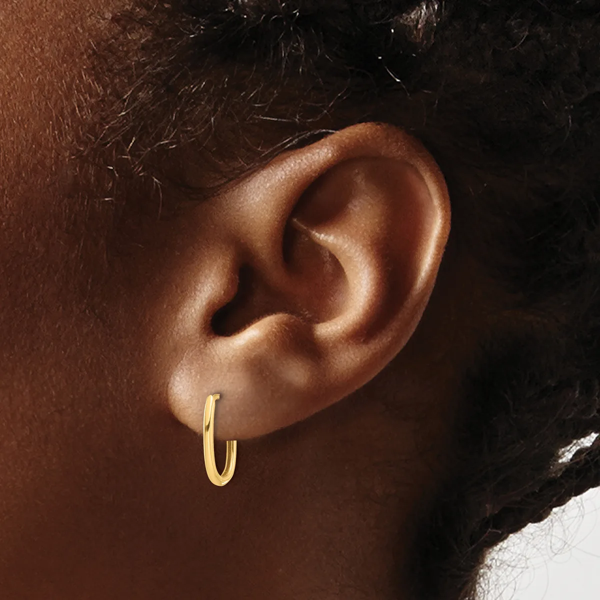 A close-up view of a person's ear wearing a small gold hoop earring against their brown skin tone.
