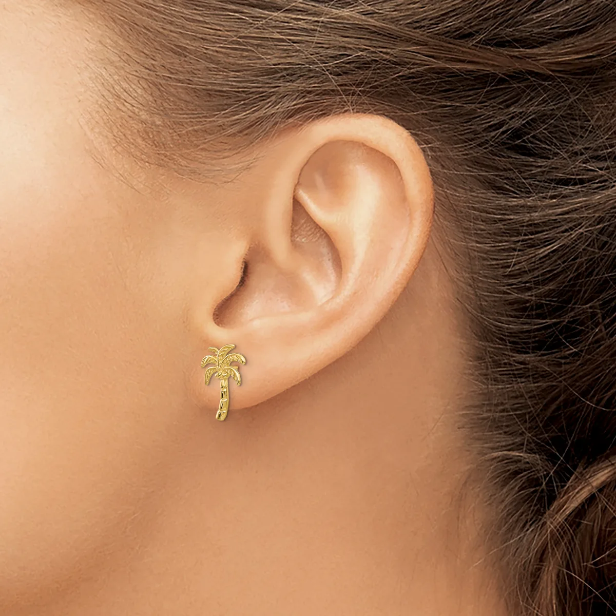 A person wearing a small gold palm tree stud earring in their earlobe, shown from the side profile.