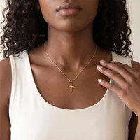 Woman wearing a white sleeveless tank top and a gold cross pendant necklace on a thin chain, with her hand resting near her chest.