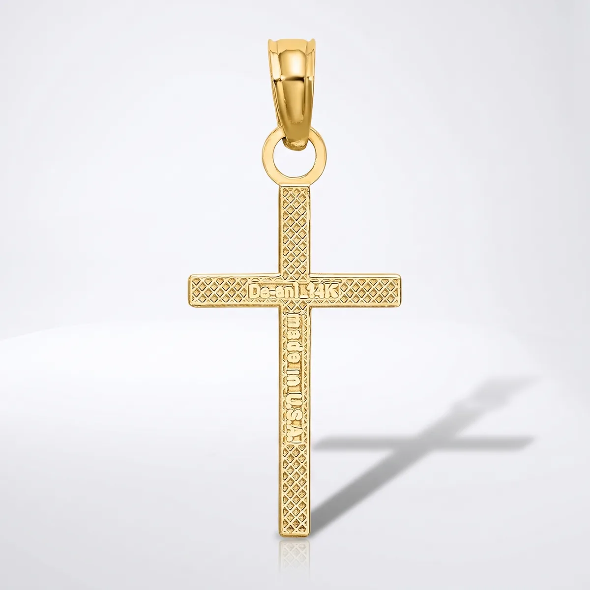 A gold cross pendant with textured surface and small hallmark, shown hanging from a bail against a white background with shadow.