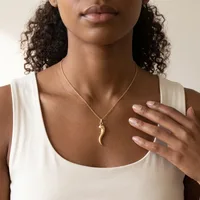 Woman wearing a white sleeveless top and a gold chain necklace with a curved horn-shaped pendant, displaying a ring on her hand.