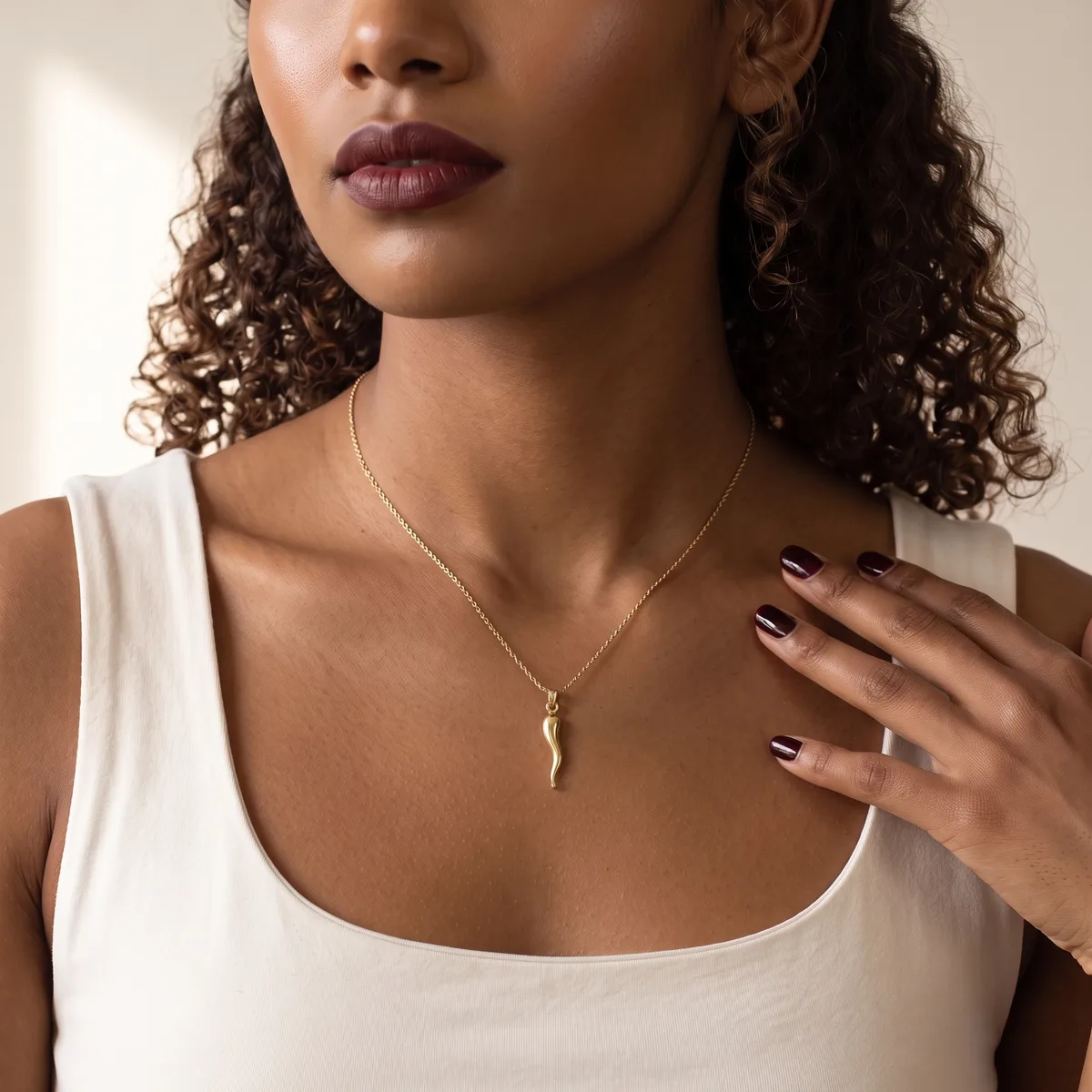 A woman wearing a white sleeveless top and a silver chain necklace with a small pendant, displaying manicured nails with dark polish.