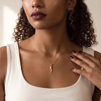 A woman wearing a white sleeveless top and a silver chain necklace with a small pendant, displaying manicured nails with dark polish.