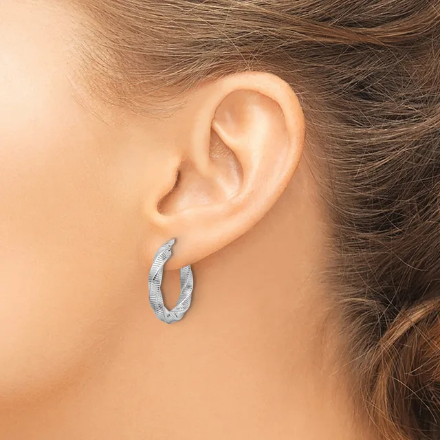 A woman wears textured silver hoop earrings on her ears, shown in profile against her neck and shoulder.