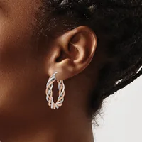 Close-up side view of a person's ear wearing a twisted oval hoop earring with a two-tone silver and rose gold finish.