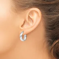 A person wearing small polished silver hoop earrings, shown from the side with their ear and part of their neck visible.