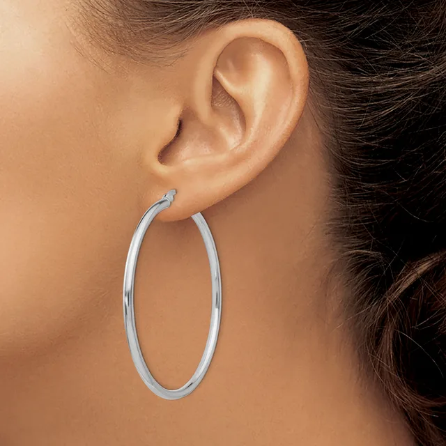 A woman wearing a pair of polished silver oval hoop earrings, shown from the side profile of her head and ear.