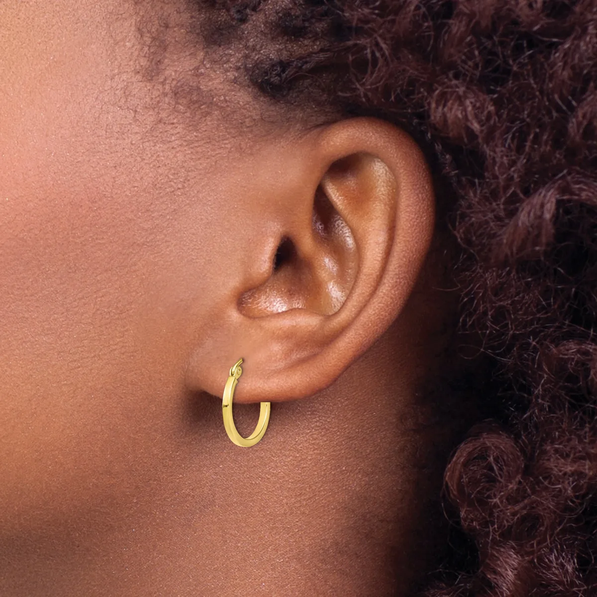 A person wearing a small gold hoop earring in their earlobe, shown in profile view against their skin.