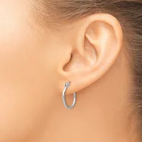 A person wearing a pair of small polished silver hoop earrings, shown from the side view of their ear and lower face.