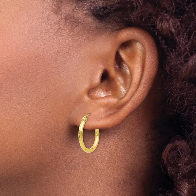 A gold hoop earring worn on the earlobe of a person with medium brown skin tone and dark curly hair.