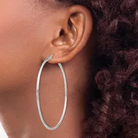 A person wearing a large oval hoop earring in polished silver metal, shown from the side profile against their neck and shoulder.