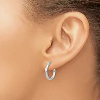 A woman wearing a polished silver curved hoop earring in her earlobe, shown from the side profile of her head and ear.