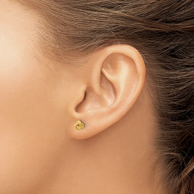 A small gold twisted knot stud earring worn in the earlobe of a person with brown hair.