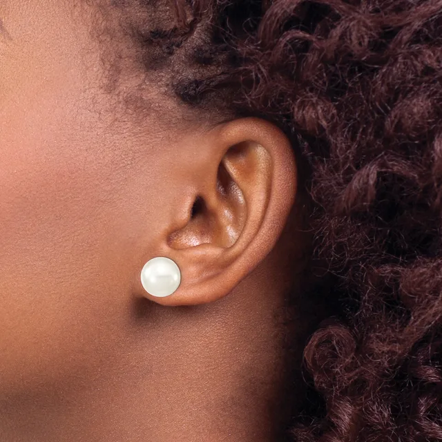 A person with deep brown skin and dark curly hair wears a white pearl stud earring in their earlobe, shown in profile from the side.