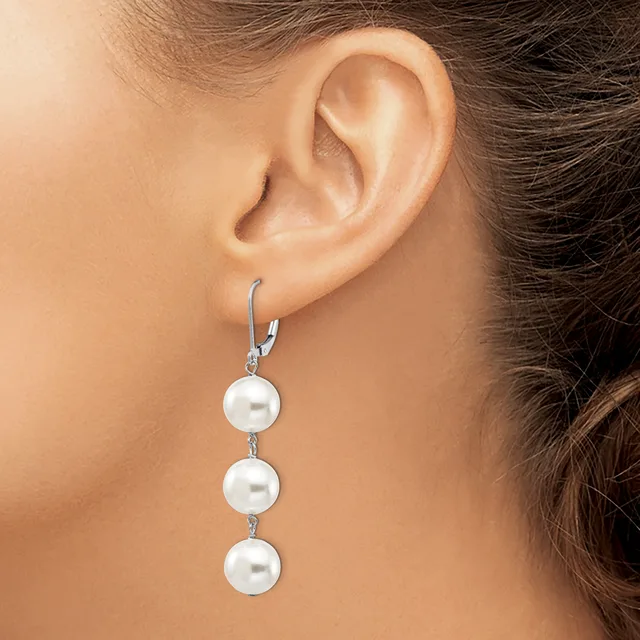 A woman wearing a silver lever-back earring with three white pearl drops suspended vertically from a chain.