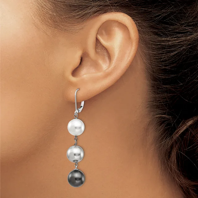 A woman wearing a dangling earring with three graduated pearl spheres in white, silver, and dark gray suspended from a silver hook clasp.