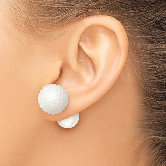 A white textured ball stud earring is worn on the earlobe of a person shown from the side, with a white backing visible below the ear.