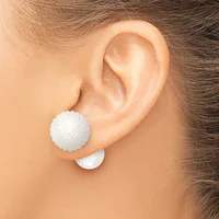 A white textured ball stud earring is worn on the earlobe of a person shown from the side, with a white backing visible below the ear.