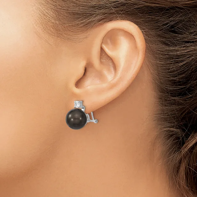 A person wearing a silver earring with a black spherical stone and rectangular clear stone accent, shown from the side view against their ear.