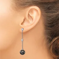 A woman wearing a long drop earring with a dark gray pearl suspended from a delicate chain adorned with small diamond accents.