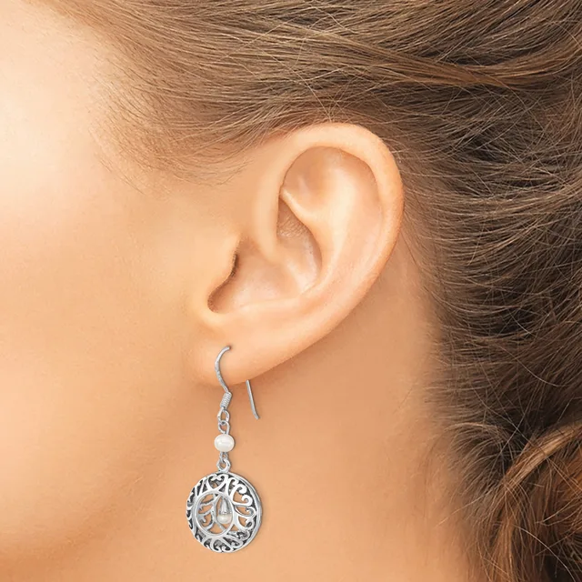 A person wearing a silver-toned dangle earring with a circular filigree pendant and a small white stone, shown from the side view of their ear.