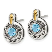 A pair of silver and gold two-tone stud earrings with round blue topaz centers surrounded by beaded borders and curved gold bail tops.
