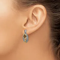 A woman wearing a two-tone oval drop earring with a textured silver outer loop and polished gold inner oval, shown from the side profile of her face and ear.