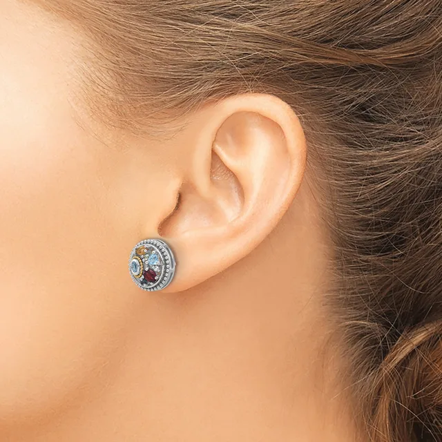 A silver stud earring with a circular design featuring blue and red gemstones surrounded by small diamonds, worn on a person's earlobe.