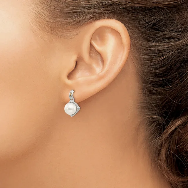 A person wearing a silver drop earring with a white pearl and diamond accents, shown from the side view of their ear and neck.