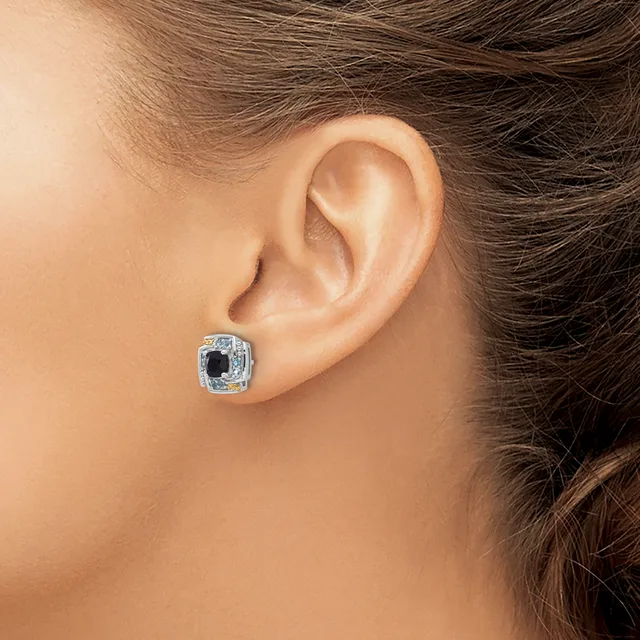 A person wearing a square cushion-cut stud earring with a dark center stone surrounded by smaller diamonds set in white metal, shown on their earlobe.