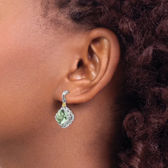 A person wearing a dangling earring with a pale green teardrop-shaped stone set in an ornate silver-toned setting with a curved hook closure.