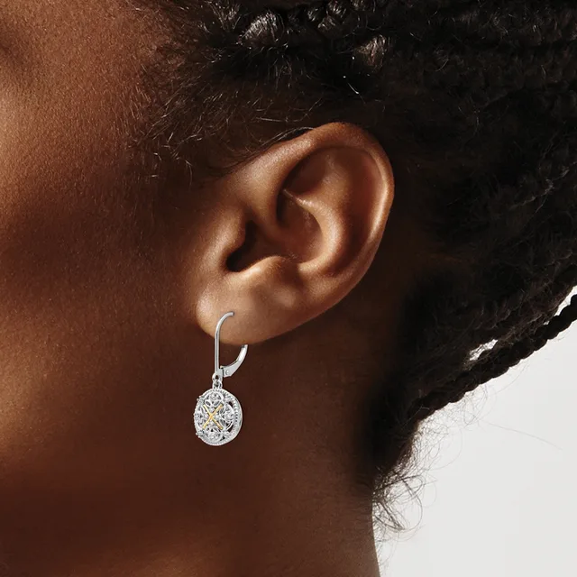 A person wearing a silver lever-back earring with an oval-shaped diamond pendant hanging from the earlobe.