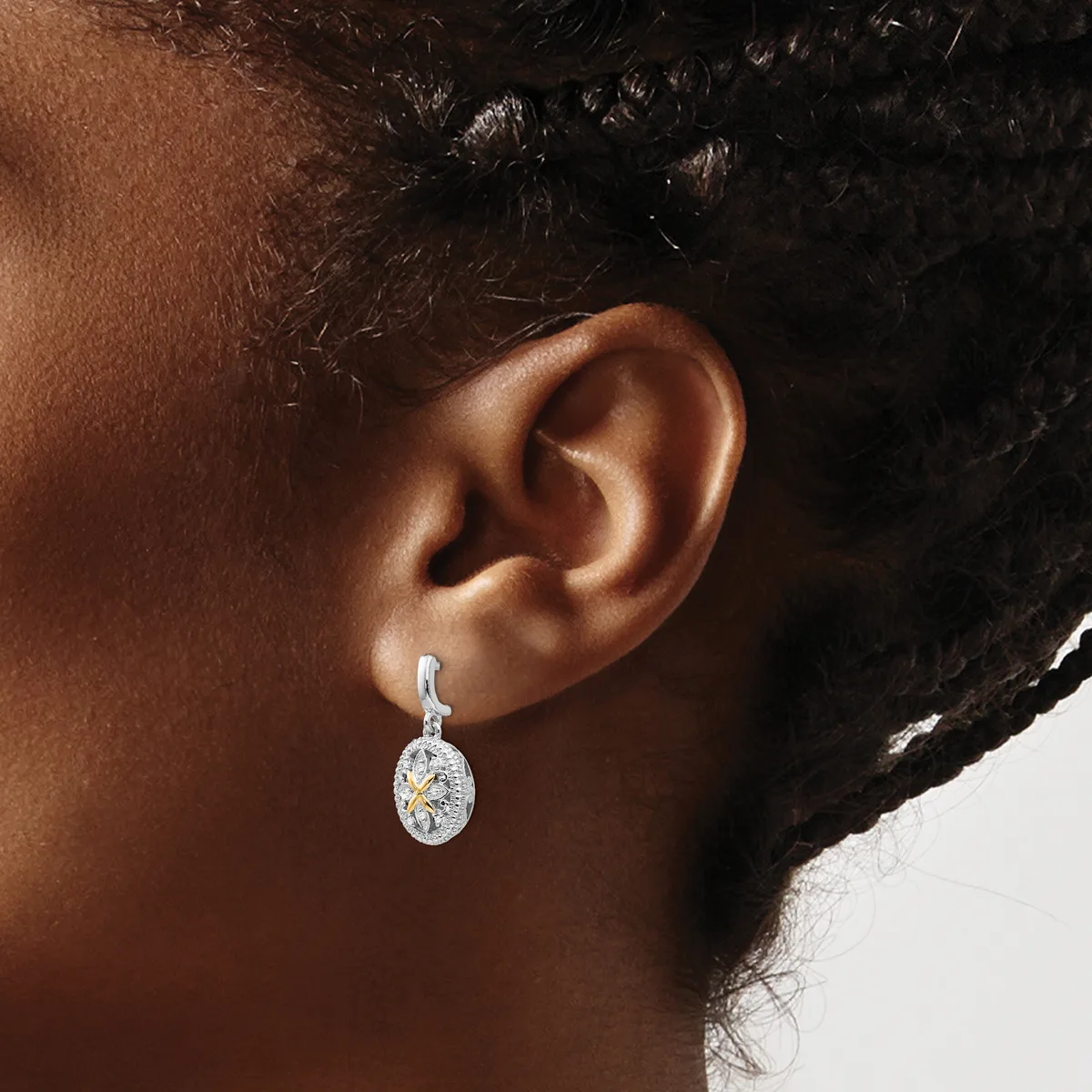 A person wearing a silver oval pendant earring with a center diamond surrounded by smaller diamonds, shown from the side view against their ear.