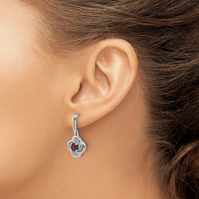 A person wearing a silver dangle earring with a twisted loop design and red gemstone accent, shown on their earlobe in profile view.