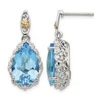 Pair of dangling earrings with large faceted blue topaz teardrop stones set in ornate silver filigree settings with gold accents on posts.