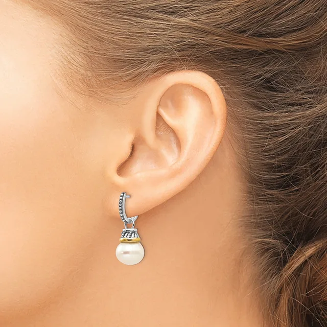 A woman wearing a silver drop earring with a decorative cap and white pearl pendant, shown from the side view near her ear.