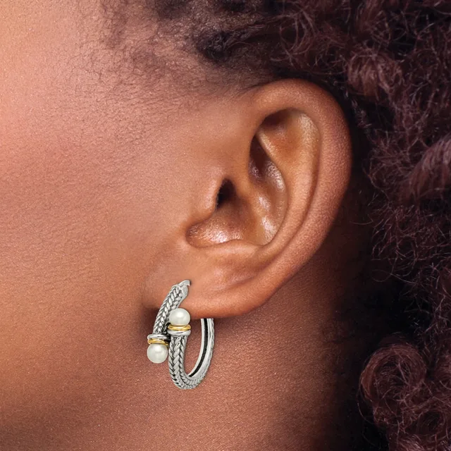 A person wearing a pair of silver textured hoop earrings with pearl accents, shown from the side profile near their ear.