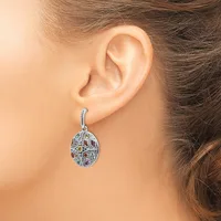 A silver drop earring with colorful gemstones hangs from a woman's earlobe.
