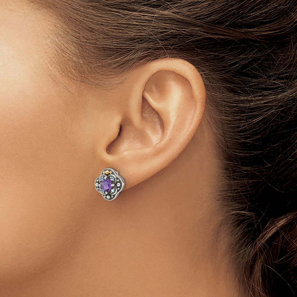 A woman wearing a silver stud earring with an amethyst stone surrounded by small round stones in a decorative square setting.