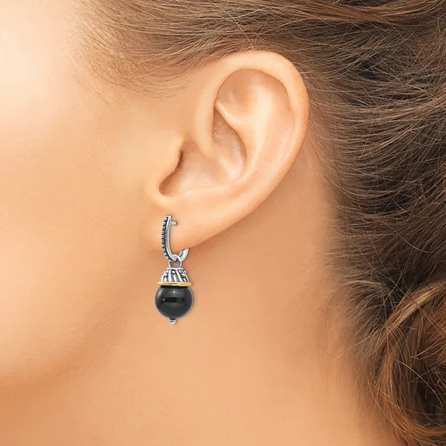 A person wearing a silver hoop earring with a decorative cap and a dangling black spherical stone or bead.