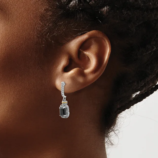 A person wearing a silver drop earring with a rectangular faceted stone and decorative bail, shown from the side profile.