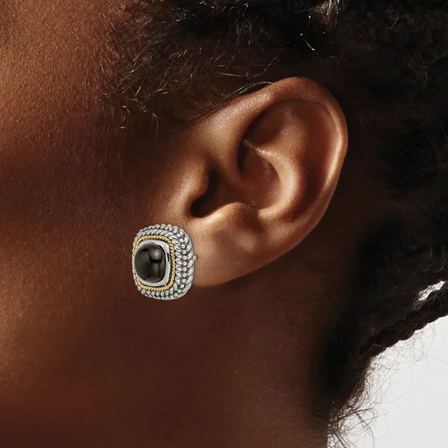 A close-up of a person's ear wearing a square stud earring with a black stone center surrounded by a textured silver-toned beaded border.