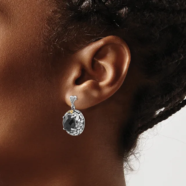 A silver drop earring with an ornate oval stone setting hangs from an earlobe.