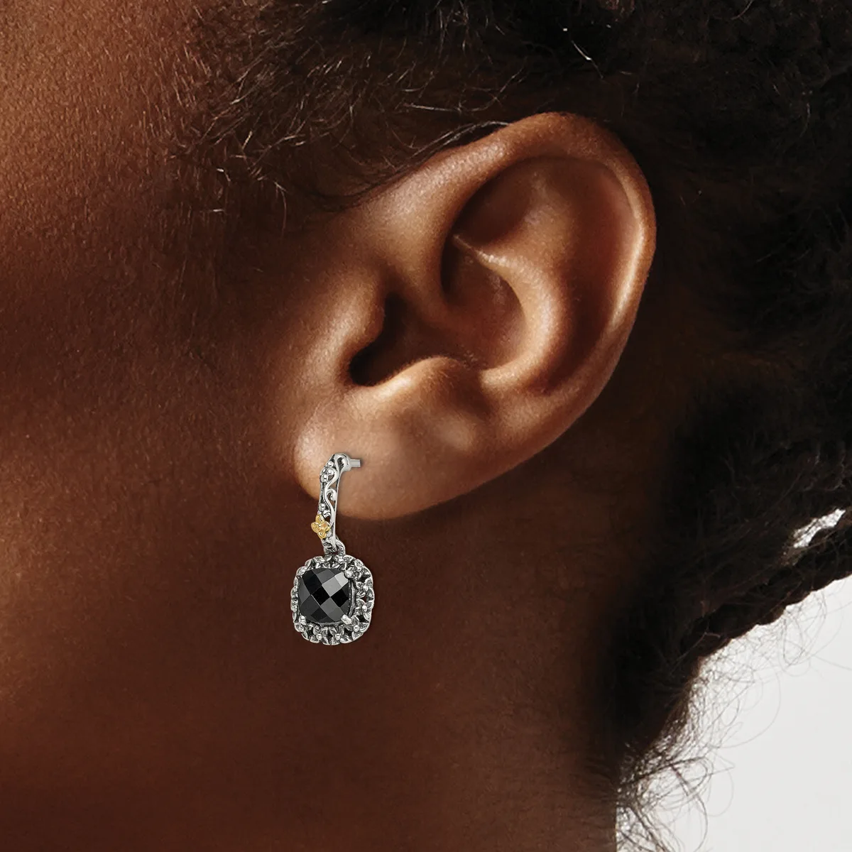 A silver drop earring with a round halo of small diamonds surrounding a larger square-cut stone, worn on a person's earlobe.